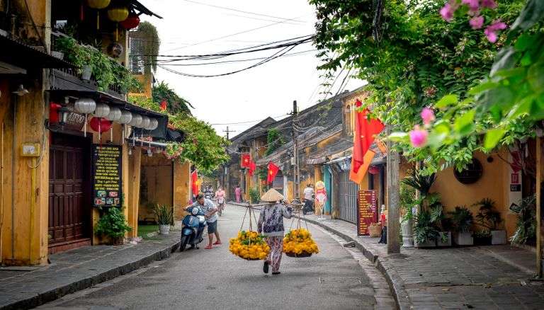 A vendor carrying flowers walks the streets of Hoi An, lined with Vietnamese flags and lanterns.