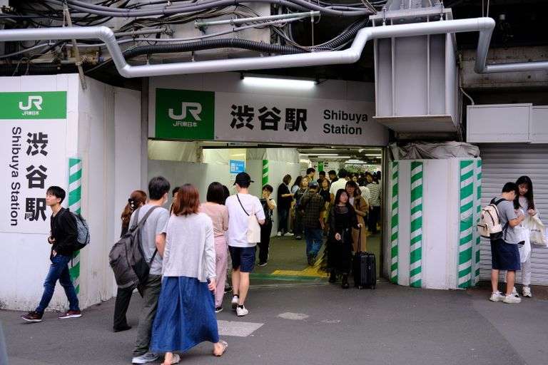 Pedestrians entering Shibuya Station in Tokyo, Japan, a bustling urban transit hub.